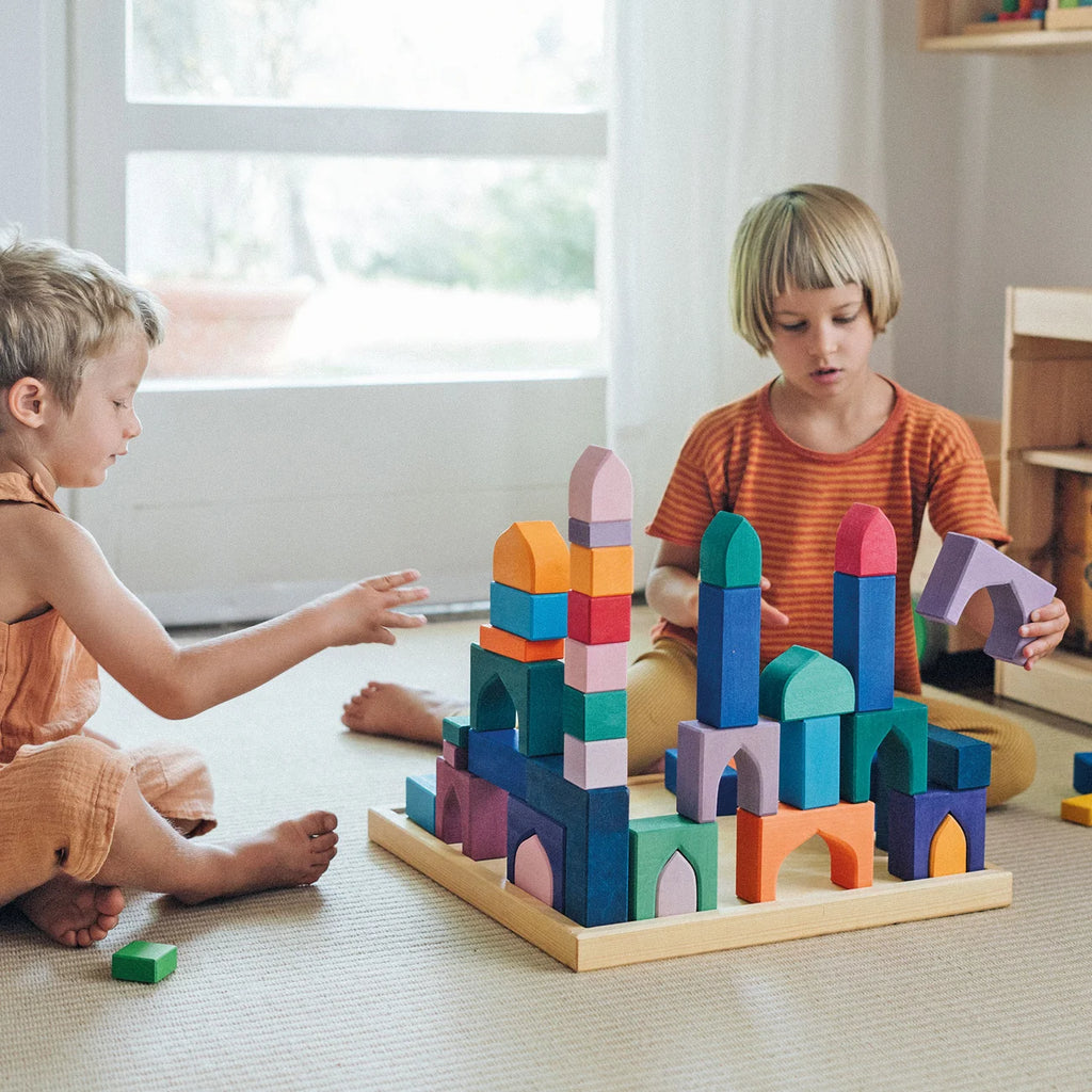 Two children playing with colorful building blocks on a light-colored floor.