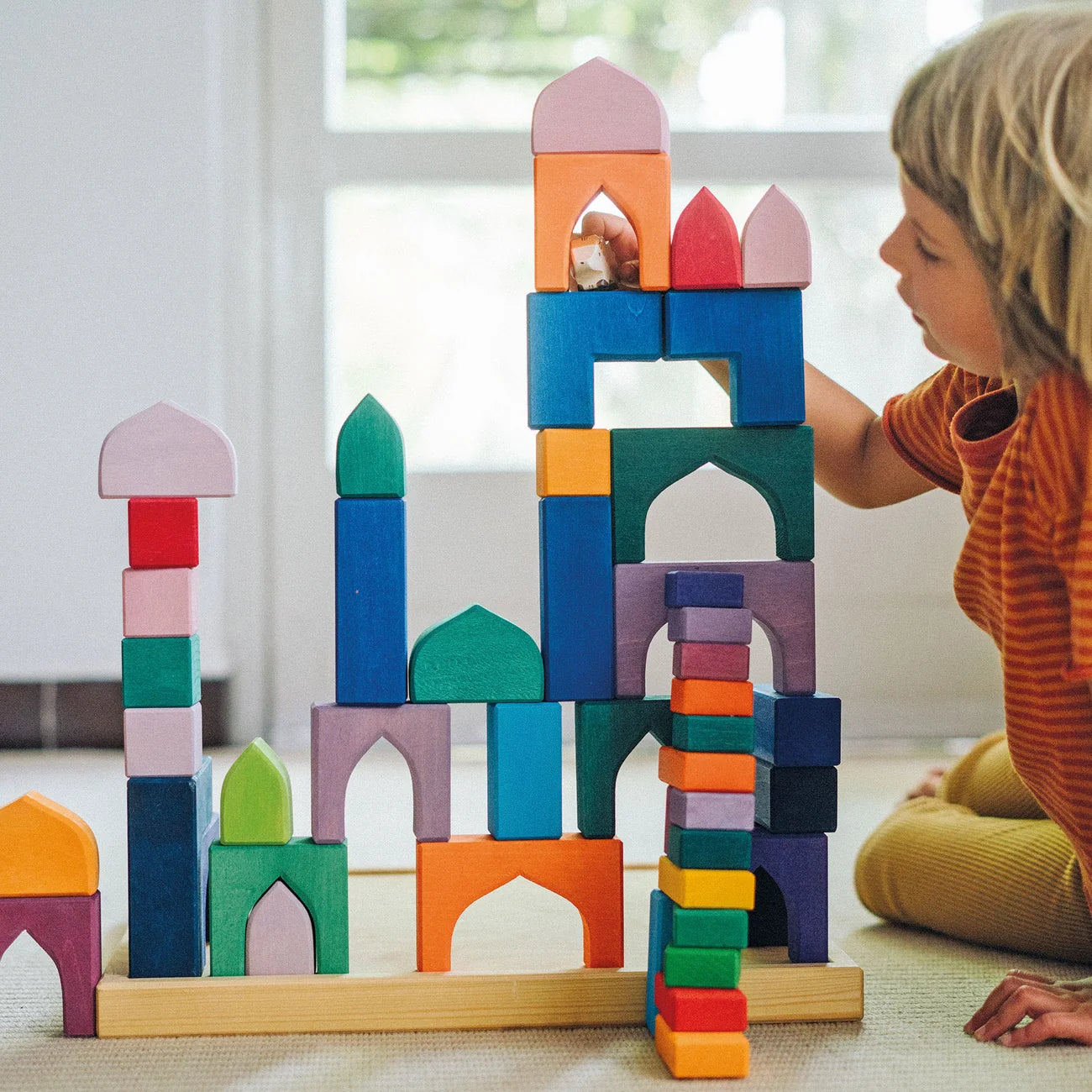 Child playing with colorful wooden building blocks on a light-colored floor.