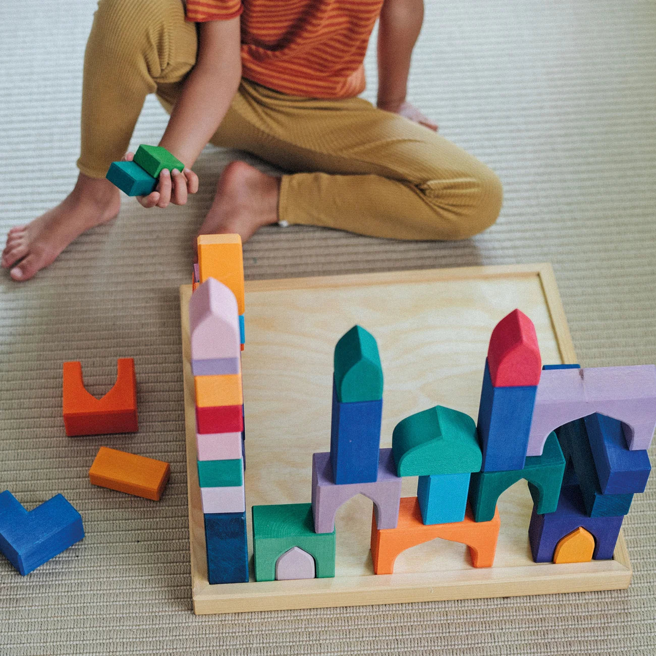 Child playing with colorful wooden building blocks on a textured floor.