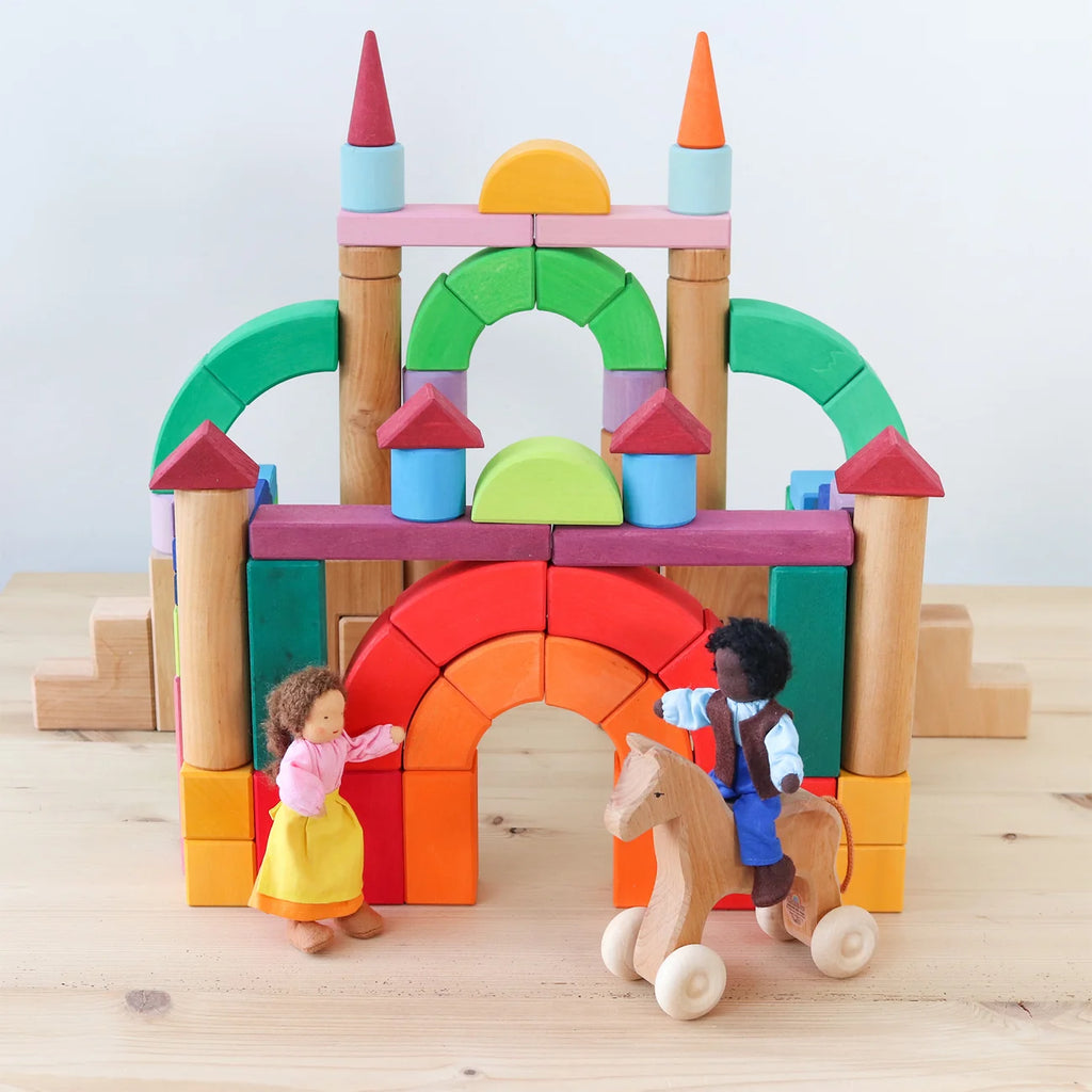 Colorful toy castle made of interlocking blocks with two small figures and a horse on a wooden surface.