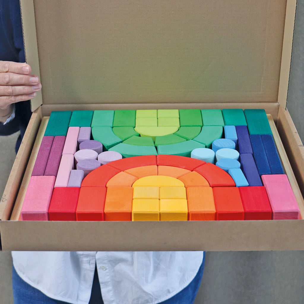 Colorful wooden blocks arranged in a rainbow pattern inside an open cardboard box.