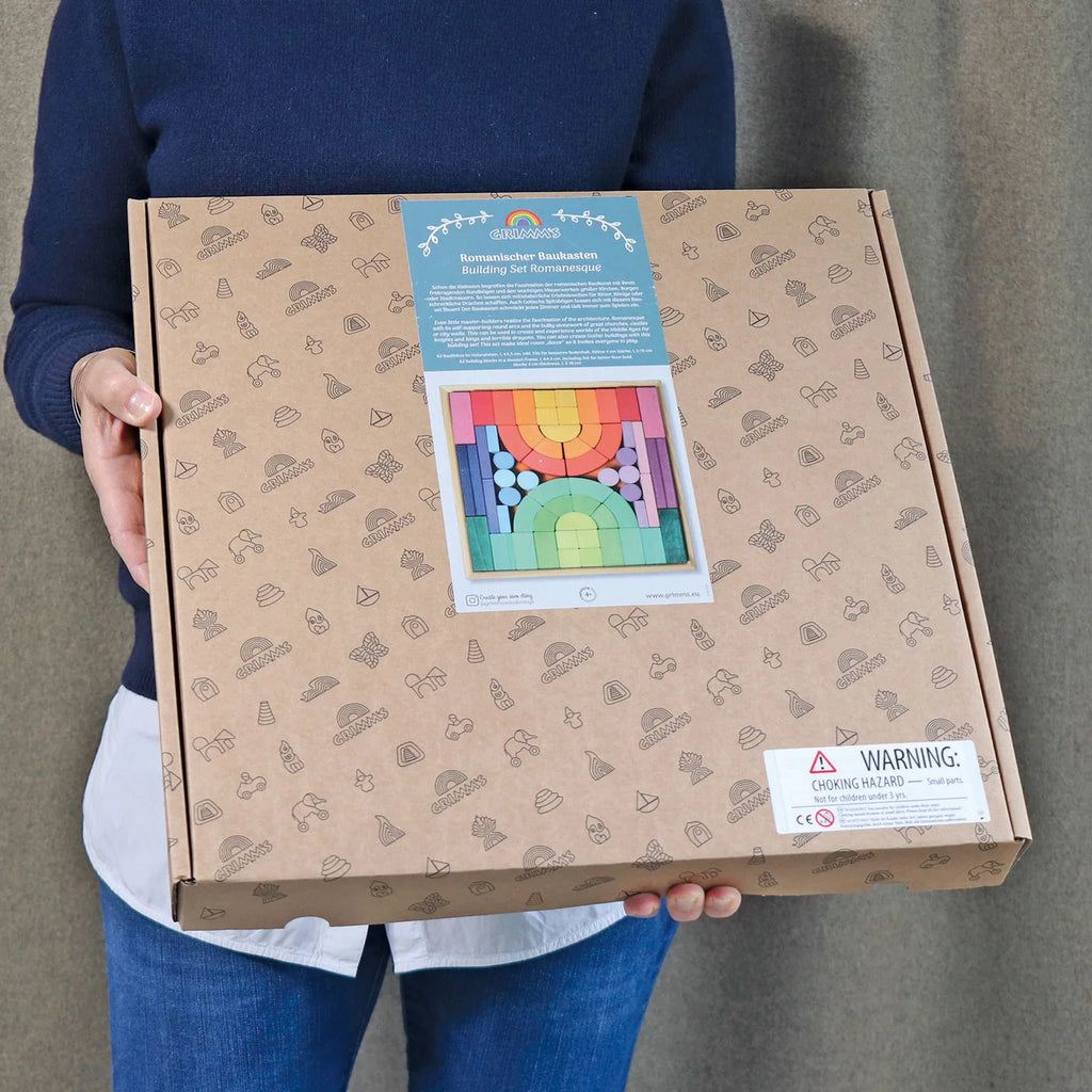 Person holding a cardboard box with a colorful product image on the label against a neutral background