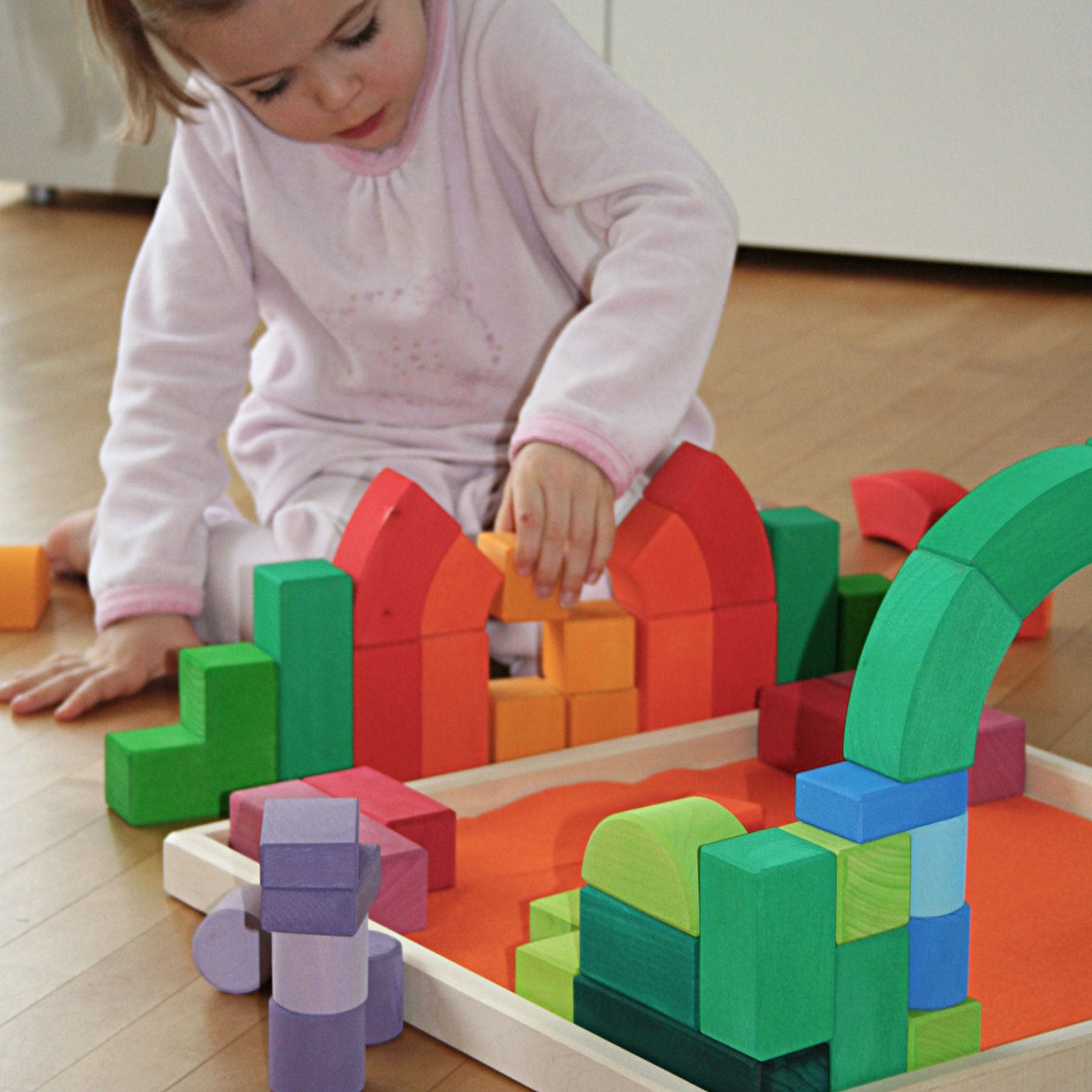 Child playing with colorful building blocks on a wooden floor