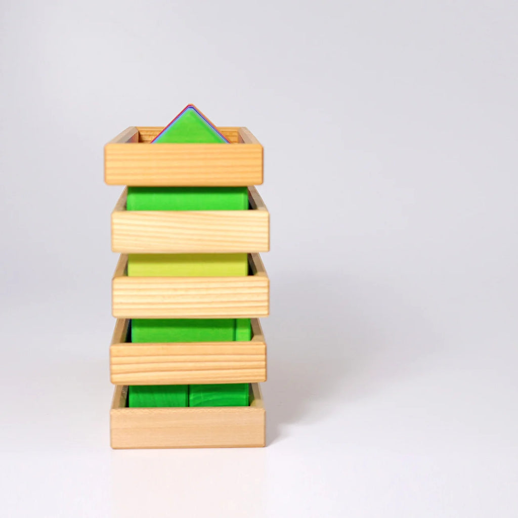 A Montessori-style wooden geometric block tower with five natural wood drawers or slots, containing green, yellow-green, and blue-green triangular and rectangular blocks, photographed on a clean white studio background.