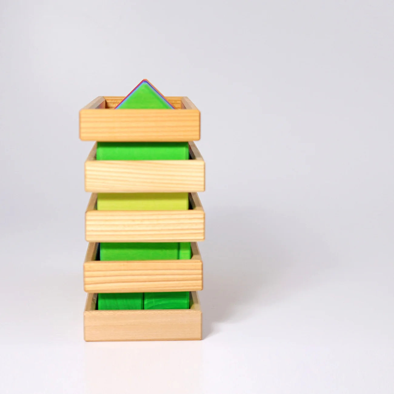 A Montessori-style wooden geometric block tower with five natural wood drawers or slots, containing green, yellow-green, and blue-green triangular and rectangular blocks, photographed on a clean white studio background.