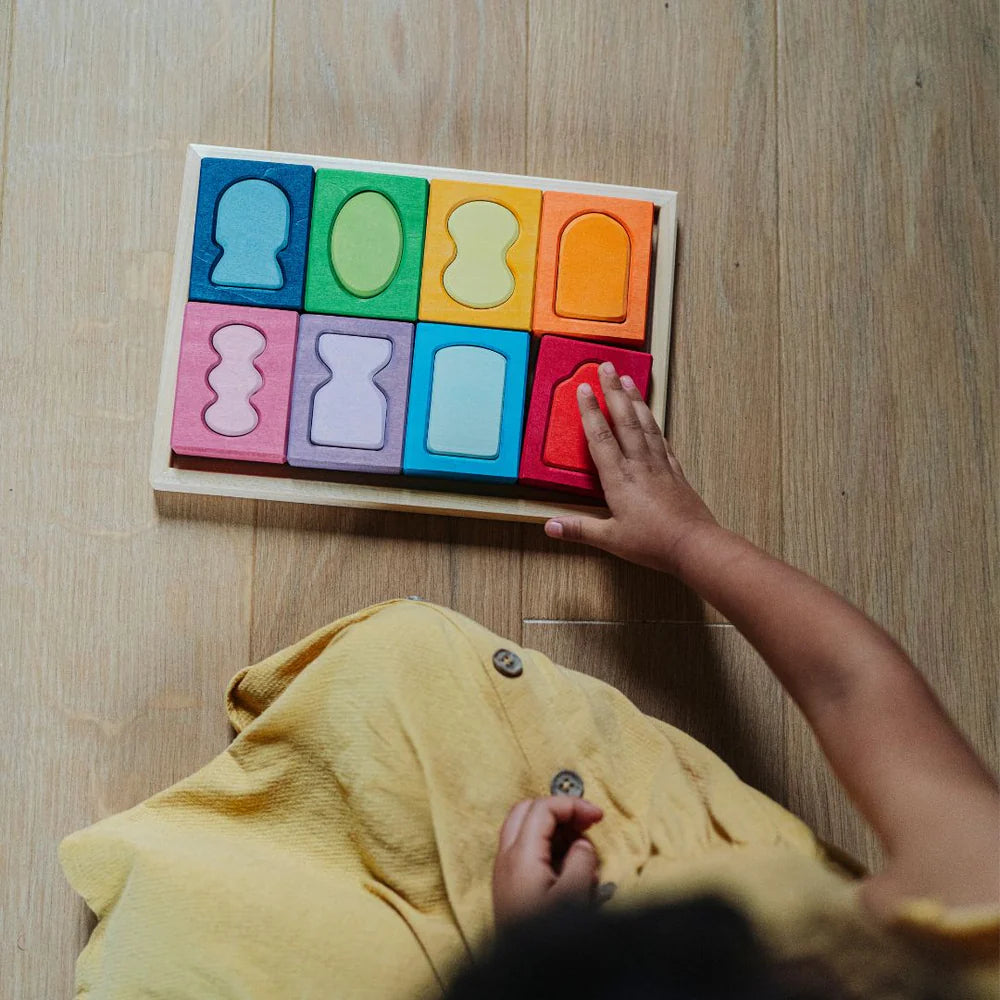 Colorful wooden block puzzle on a wooden floor with a child's hand reaching towards it.