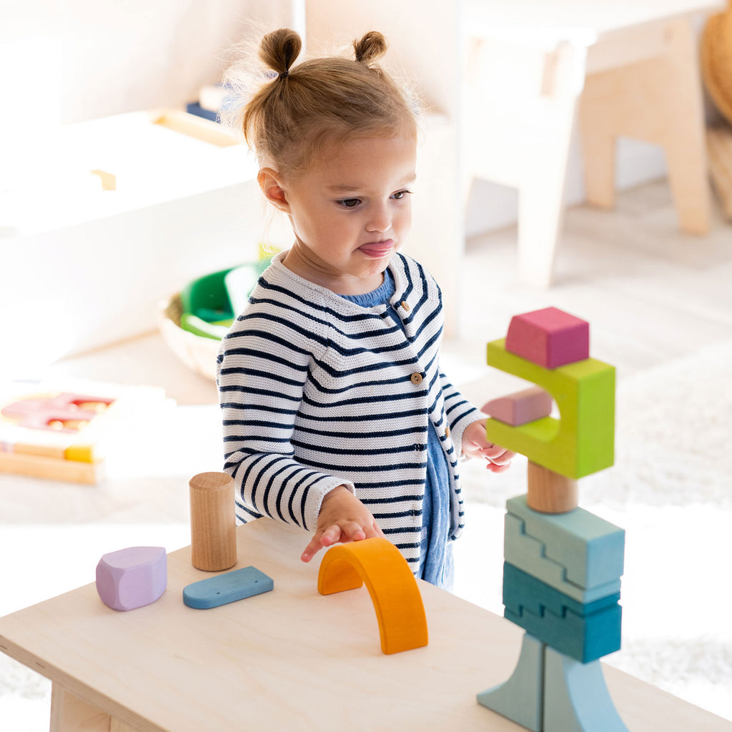 Child playing with colorful wooden blocks on a table in a bright room.