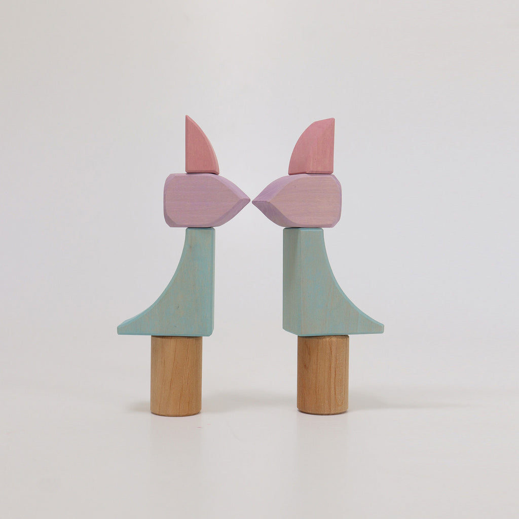 Two wooden toys with pink and green shapes on a white background