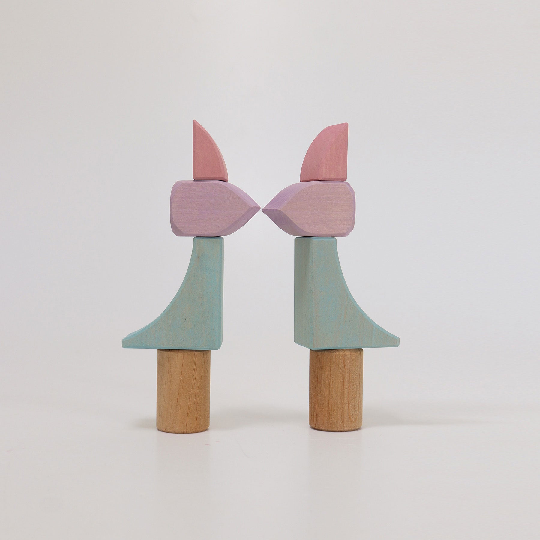 Two wooden toys with pink and green shapes on a white background