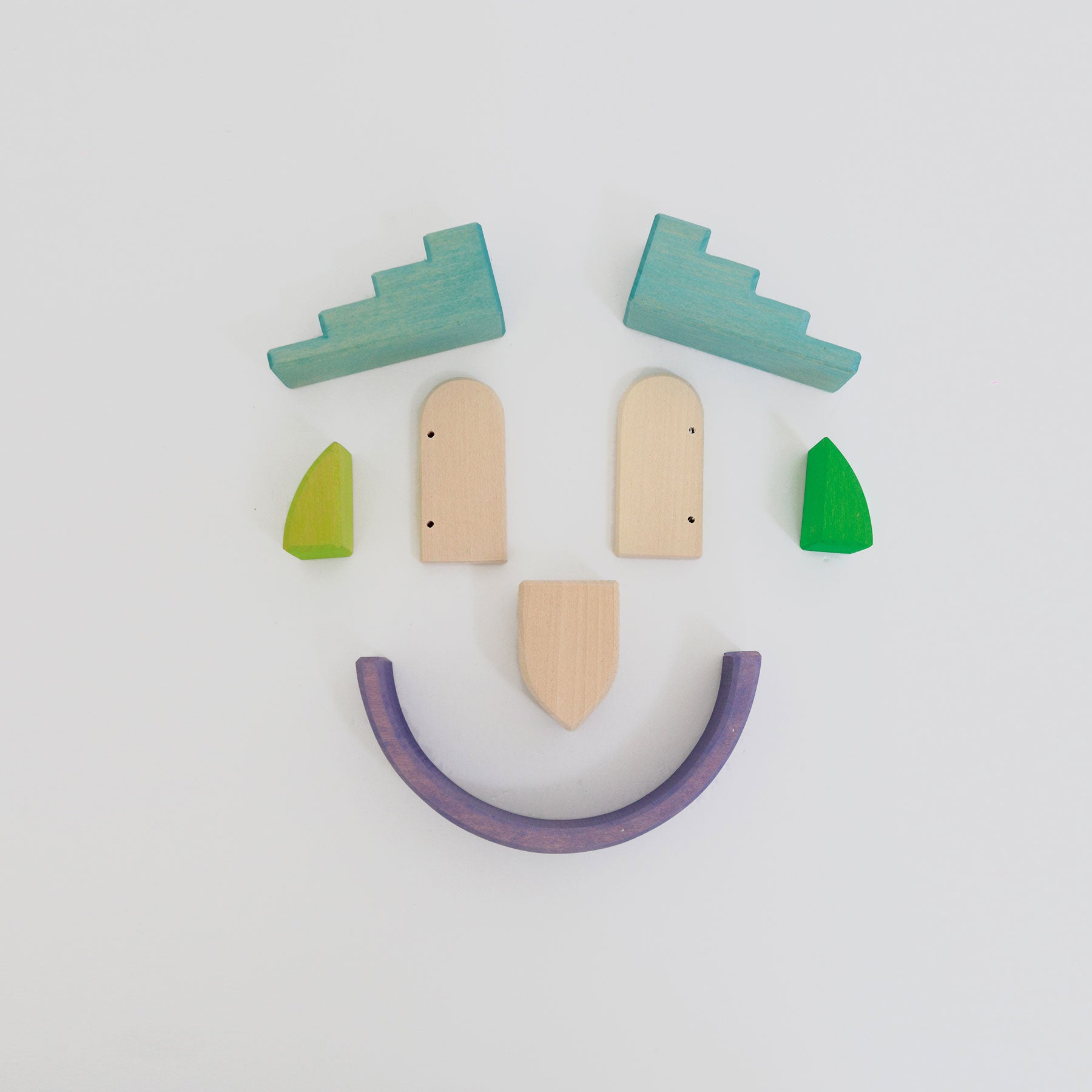 Wooden toy face with green eyes, beige nose and mouth, and purple smile on a white background