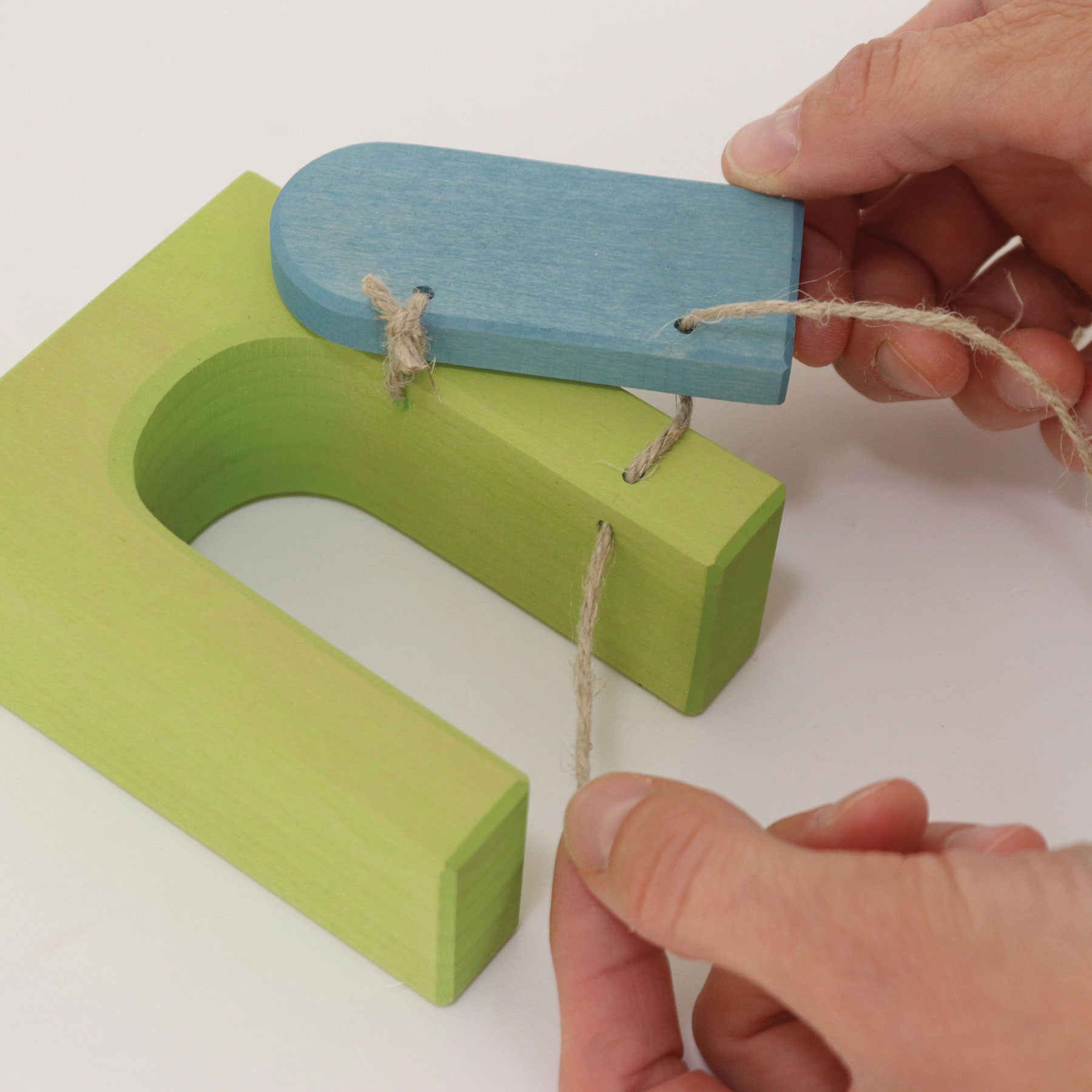 Green and blue wooden toy with string, held by a hand on a white background