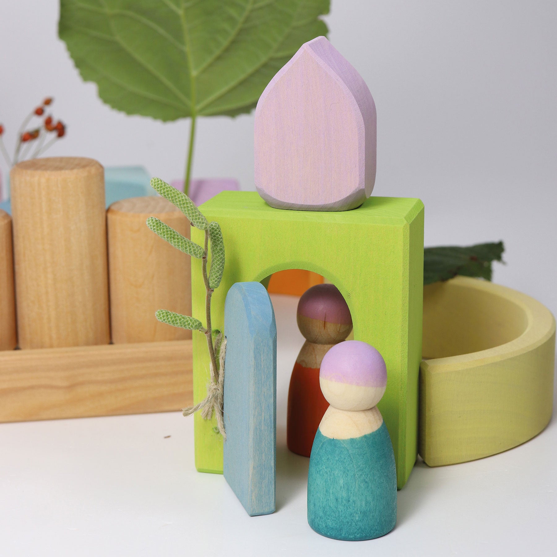 Set of colorful wooden peg dolls with a green base and leaf-shaped object on a light background.
