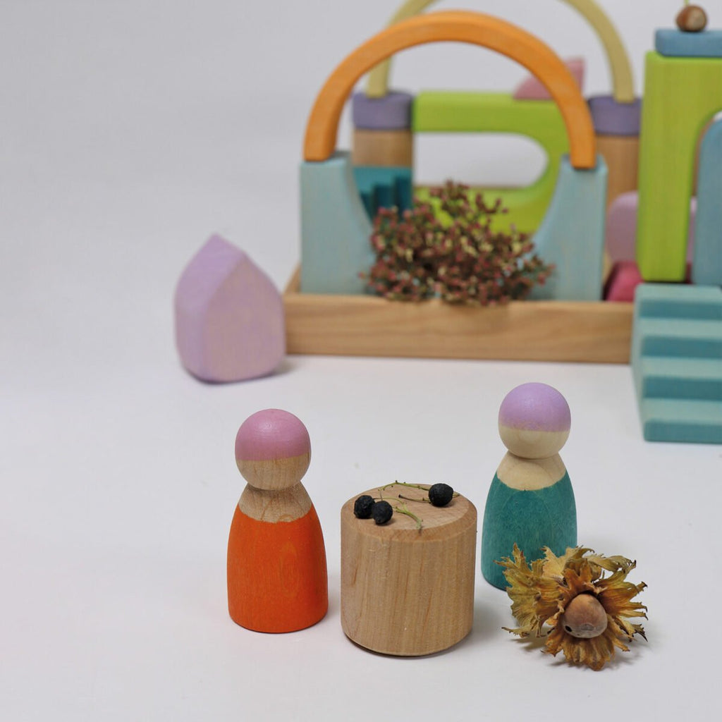 Colorful wooden peg dolls with a small wooden table and decorative items on a white background