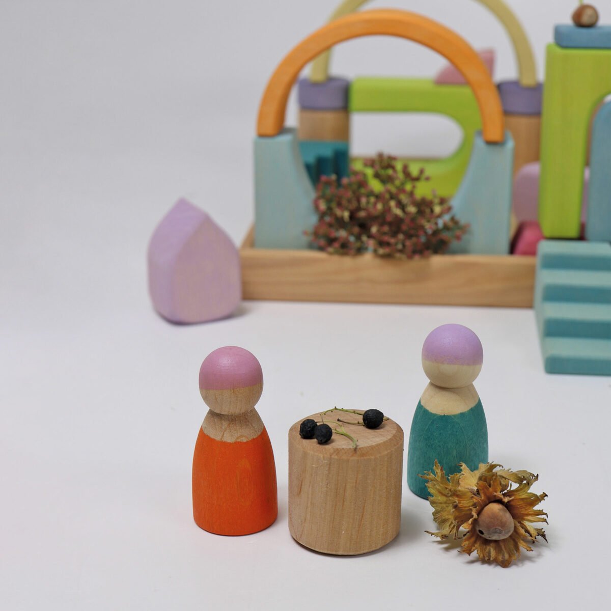 Colorful wooden peg dolls with a small wooden table and decorative items on a white background