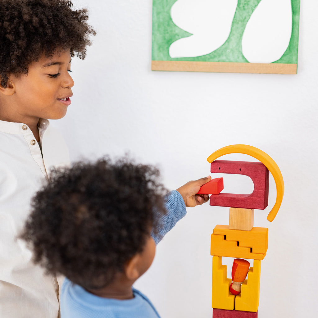 Two children playing with a colorful wooden toy on a white wall.