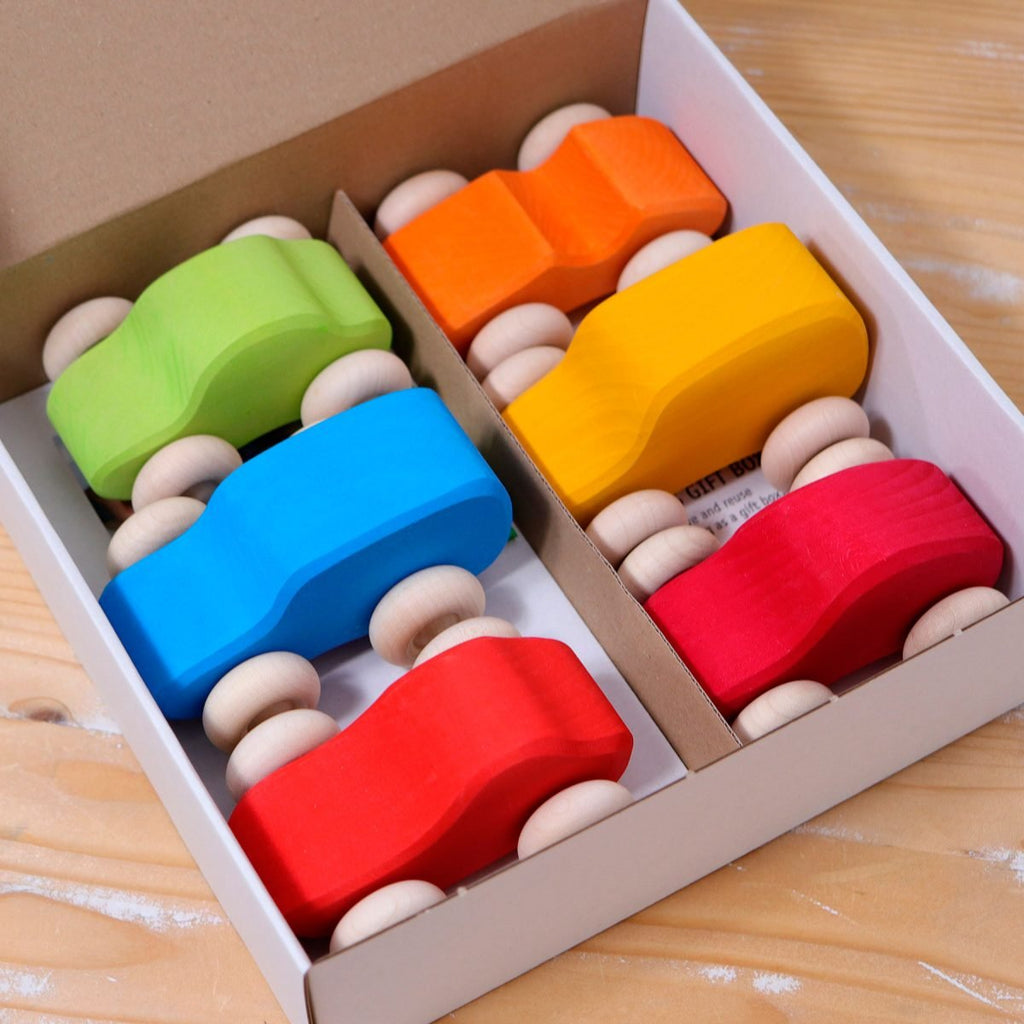 Colorful wooden toy cars in a box on a wooden surface