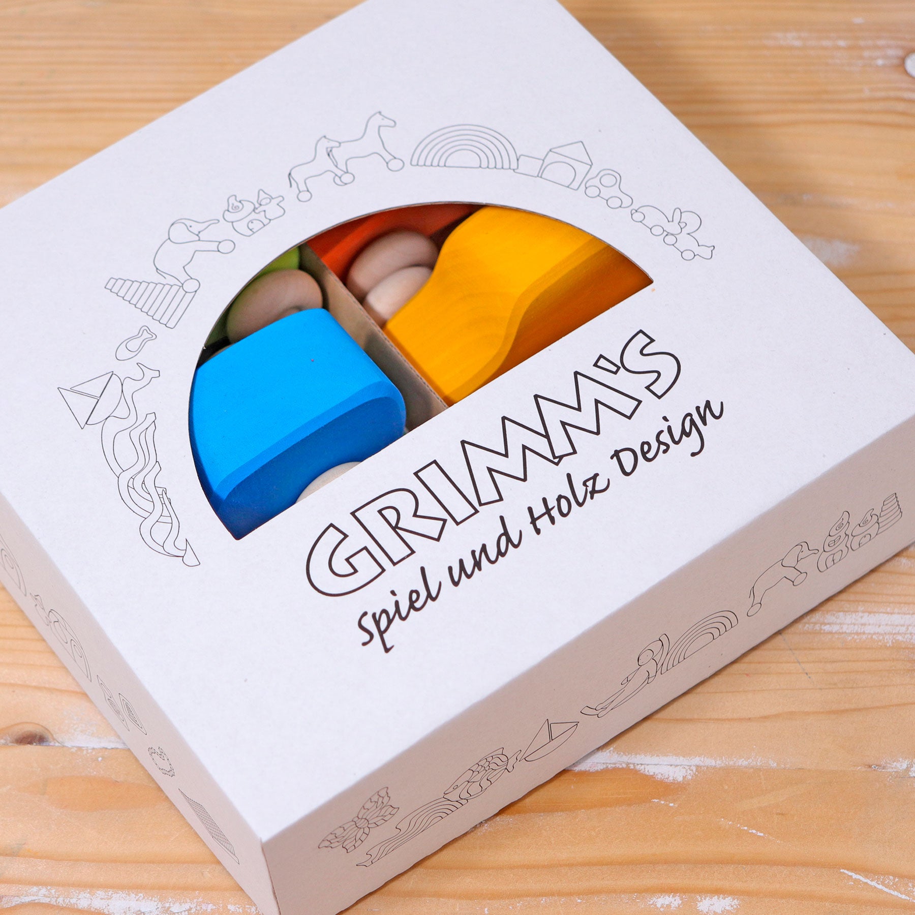 GRIMM'S Spiel und Holz Design packaging with blue and yellow wooden toys on a wooden surface