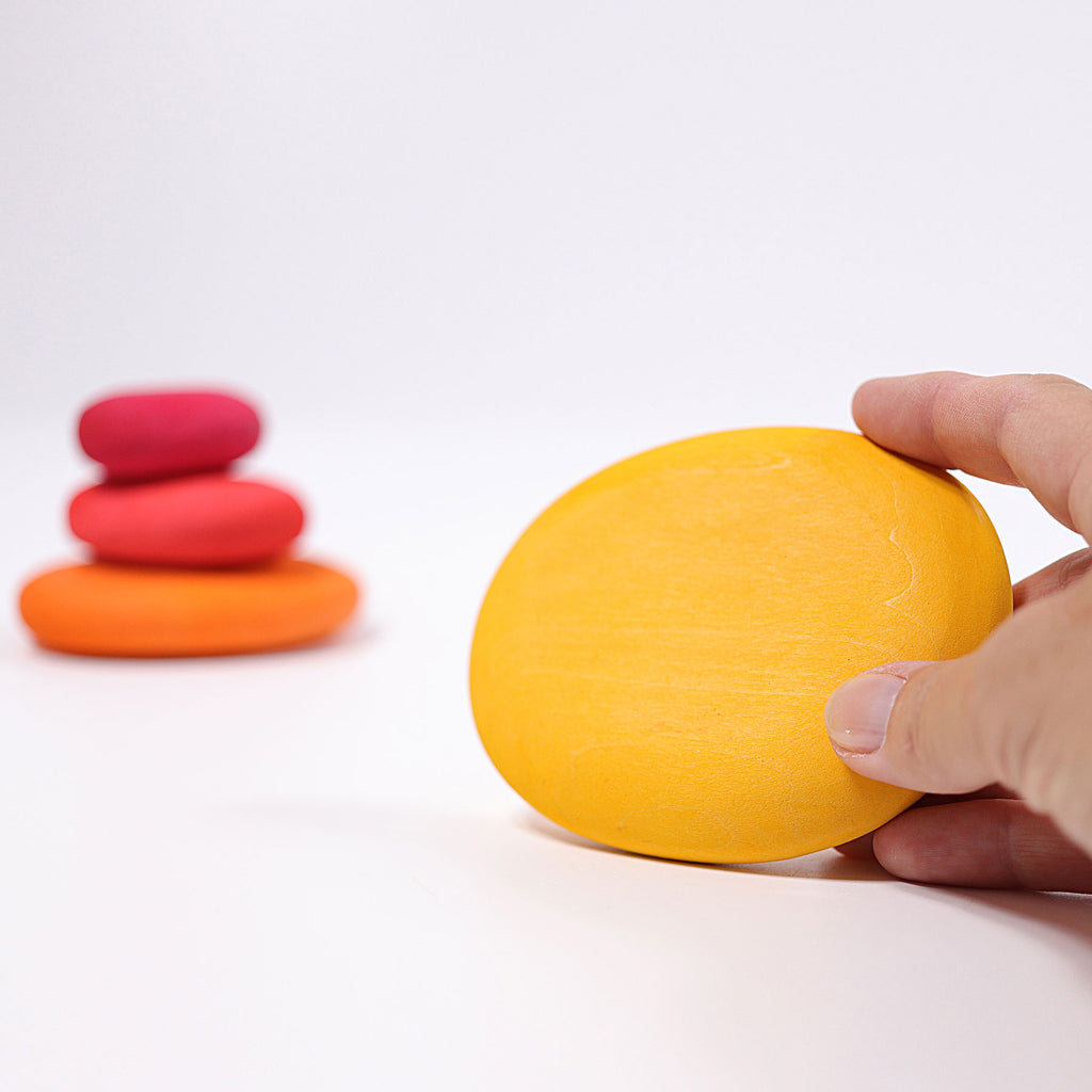 Hand holding a yellow object with colorful objects stacked in the background on a white surface
