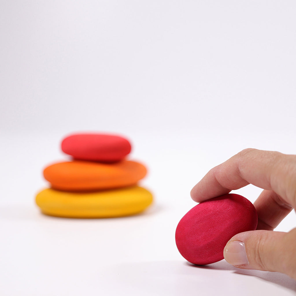 Colorful stacking stones with a hand reaching to pick up a red stone on a white background