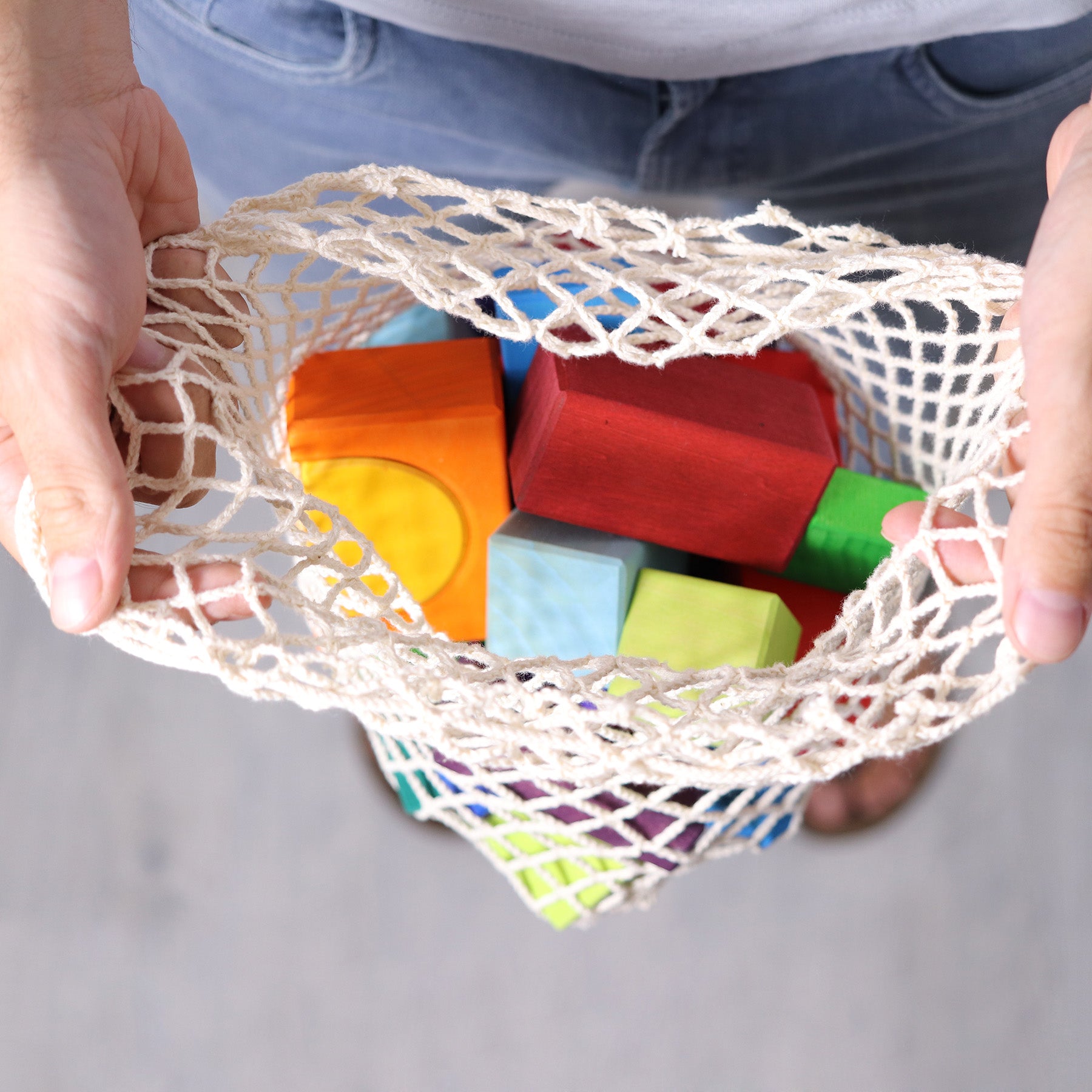 Colorful wooden blocks in a mesh bag held by hands against a neutral background
