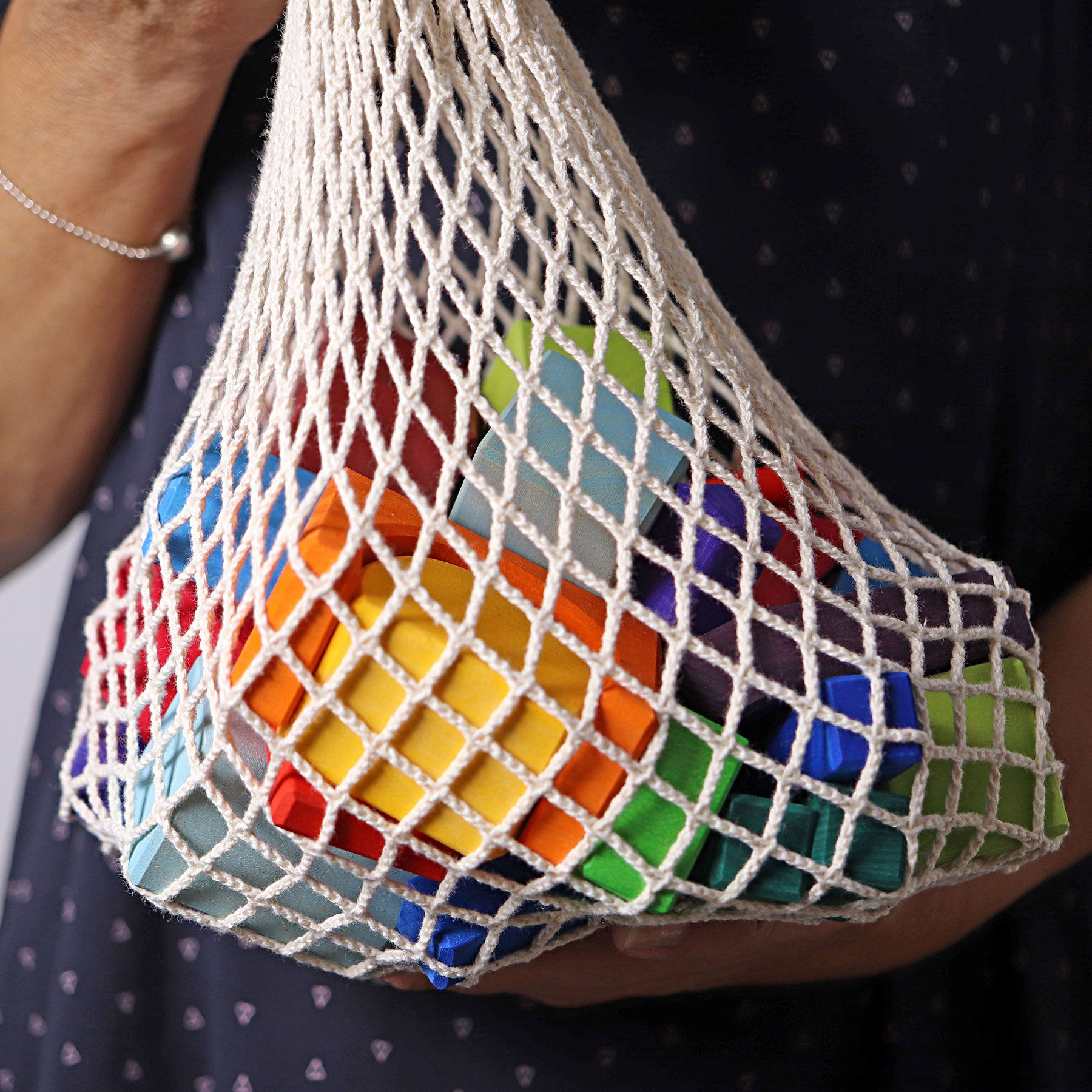 Colorful wooden blocks in a mesh bag held by a person