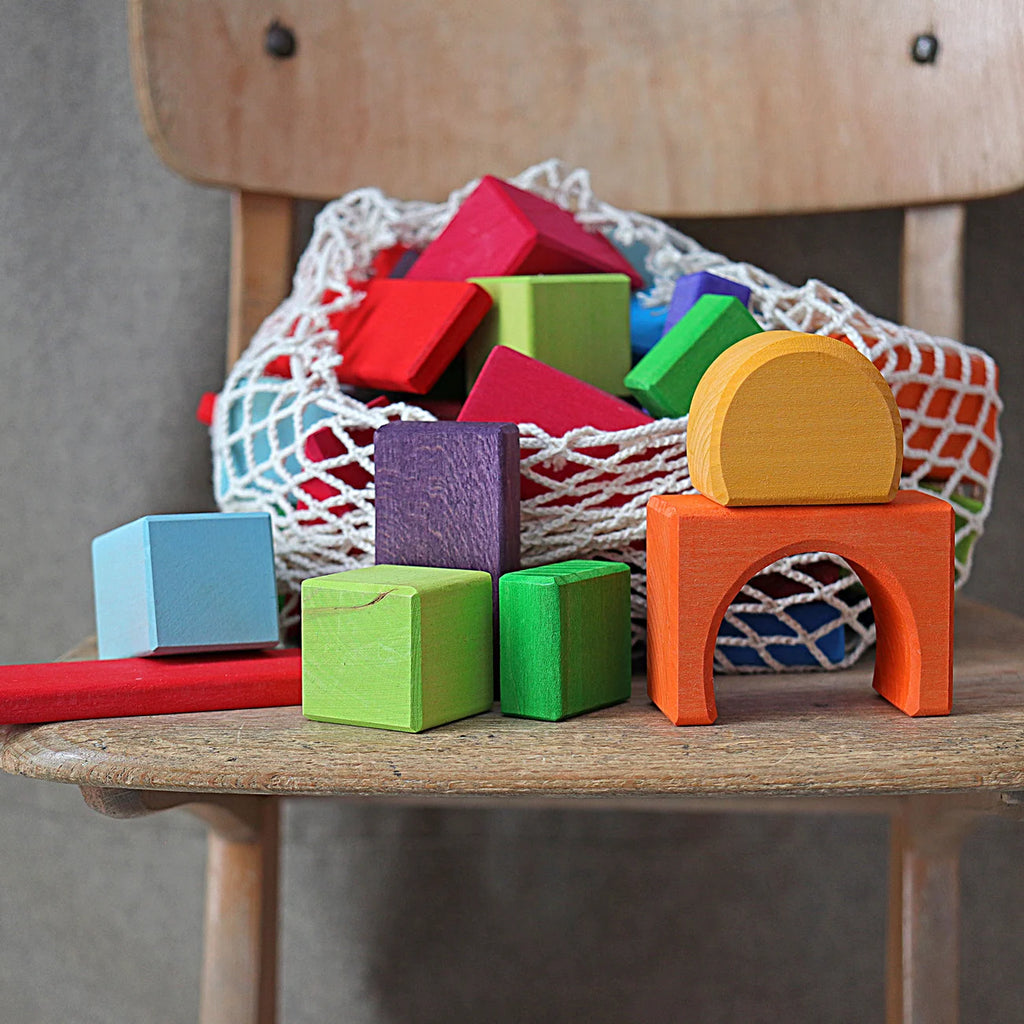 Colorful wooden blocks on a wooden surface with a bag of more blocks in the background.