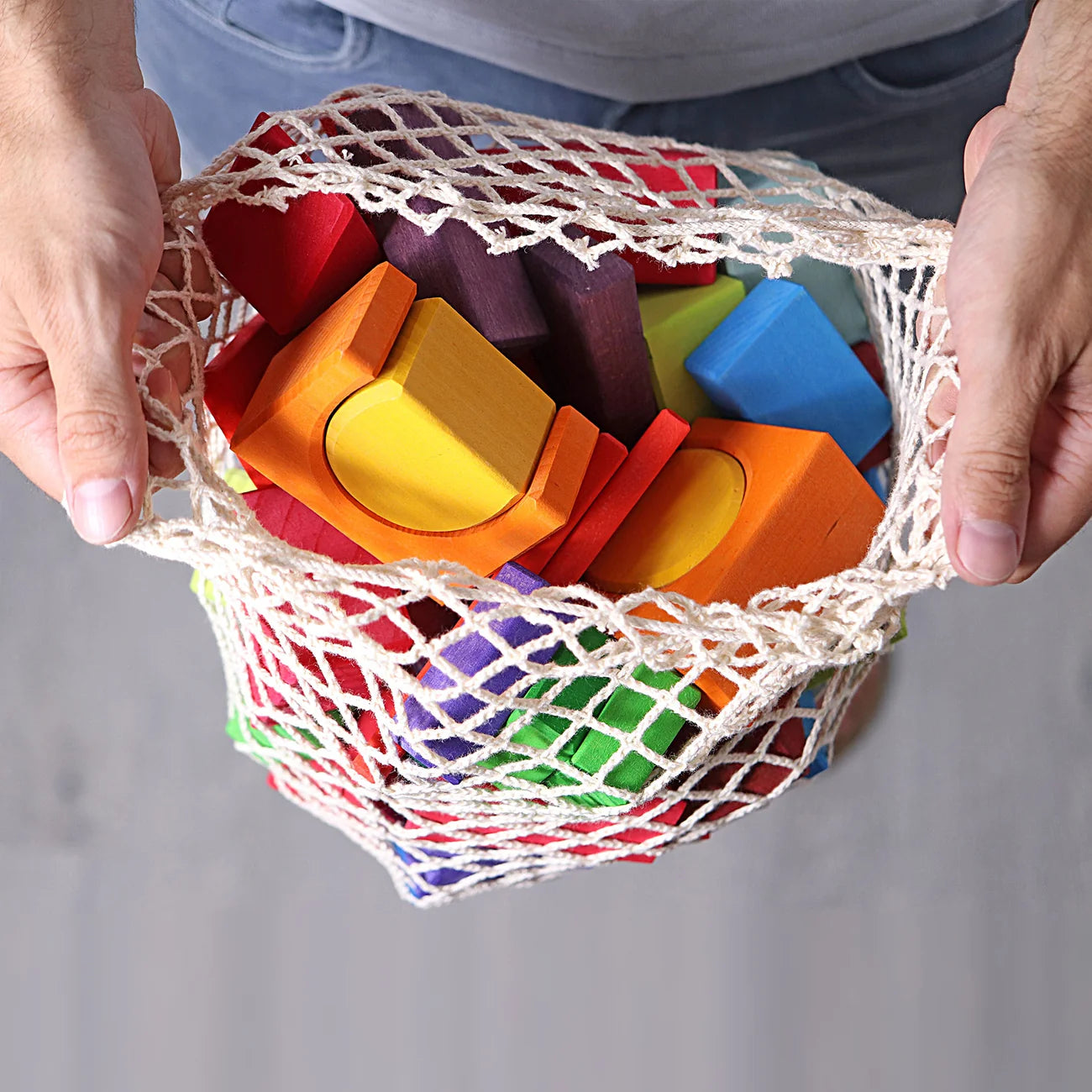 Colorful wooden blocks in a mesh bag held by hands against a neutral background