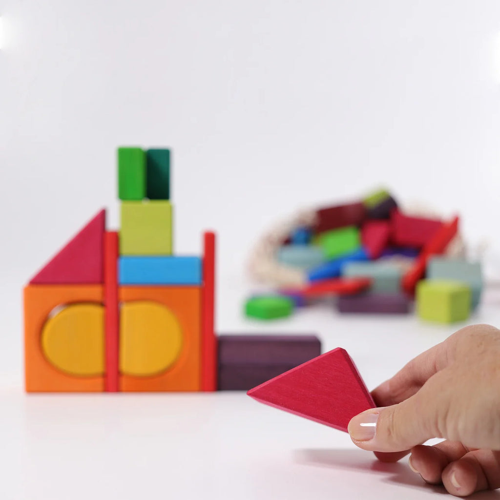 Colorful building blocks with a hand holding a red triangle block on a white background