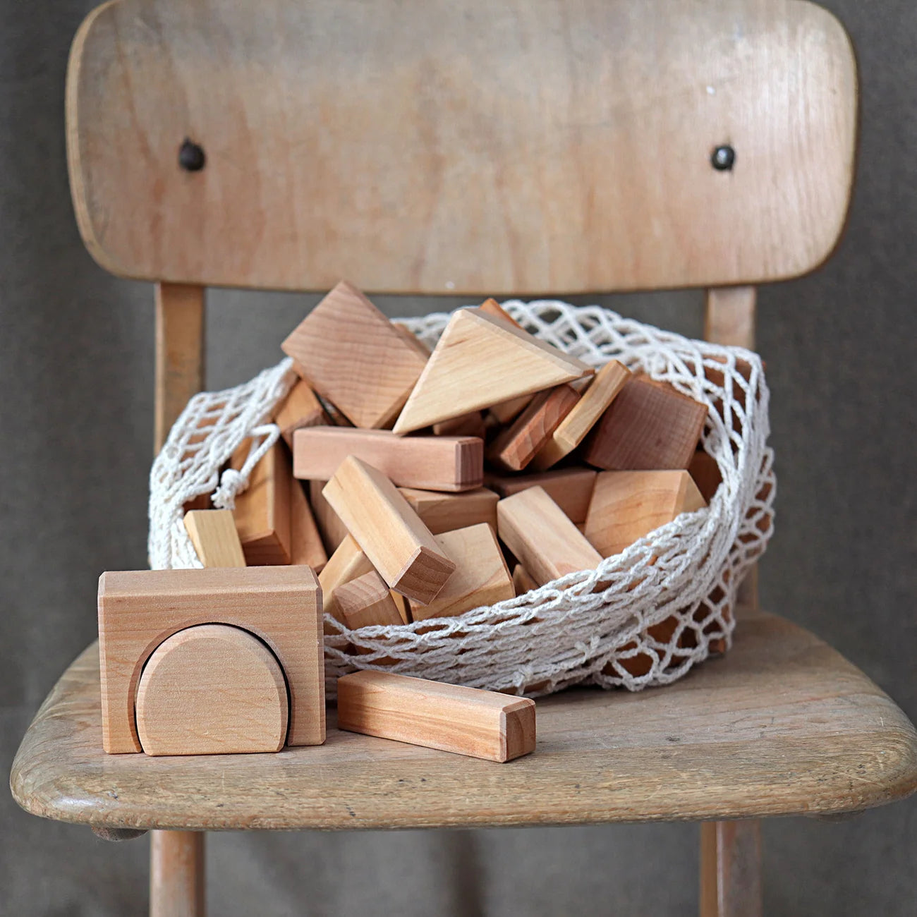 Wooden blocks in a woven basket on a wooden chair with a neutral background