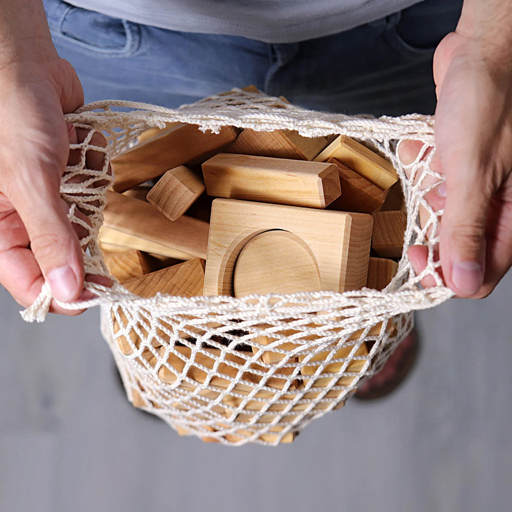 Wooden blocks in a mesh bag held by hands against a neutral background