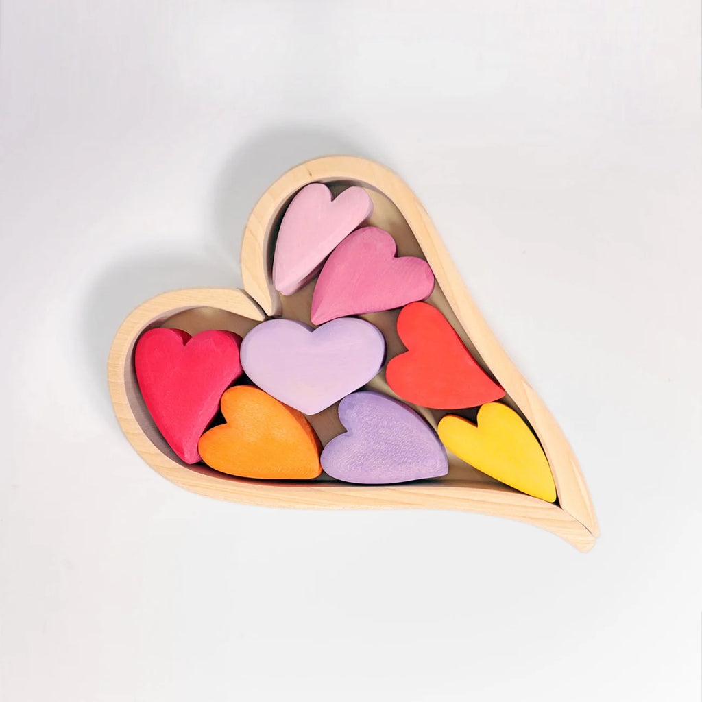 A wooden heart-shaped tray holding multiple small pastel and bright heart shapes in pink, purple, red, orange, and yellow, photographed on a clean white background.