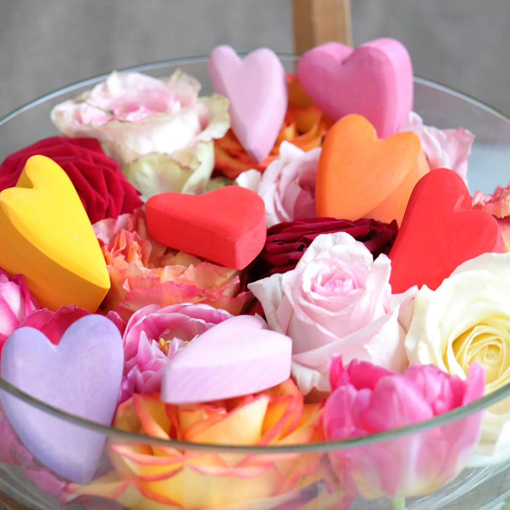 Glass bowl filled with colorful flowers and heart-shaped objects on a neutral background