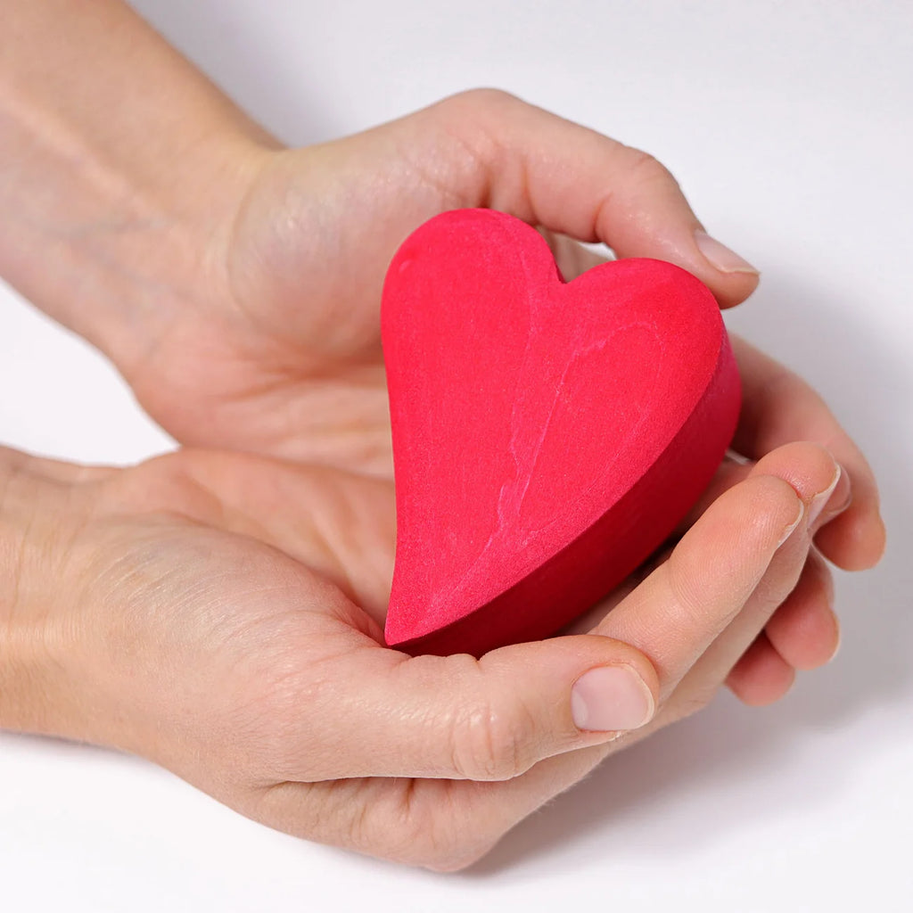Red heart-shaped object held in a hand against a white background