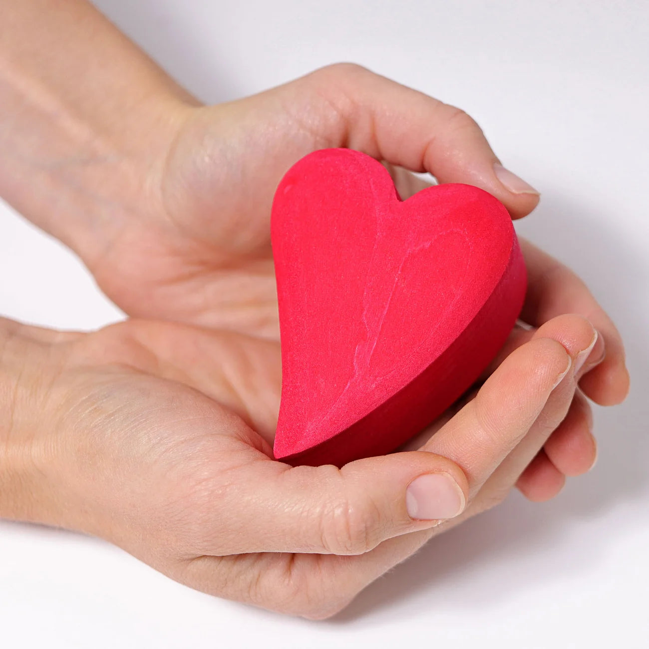 Red heart-shaped object held in a hand against a white background