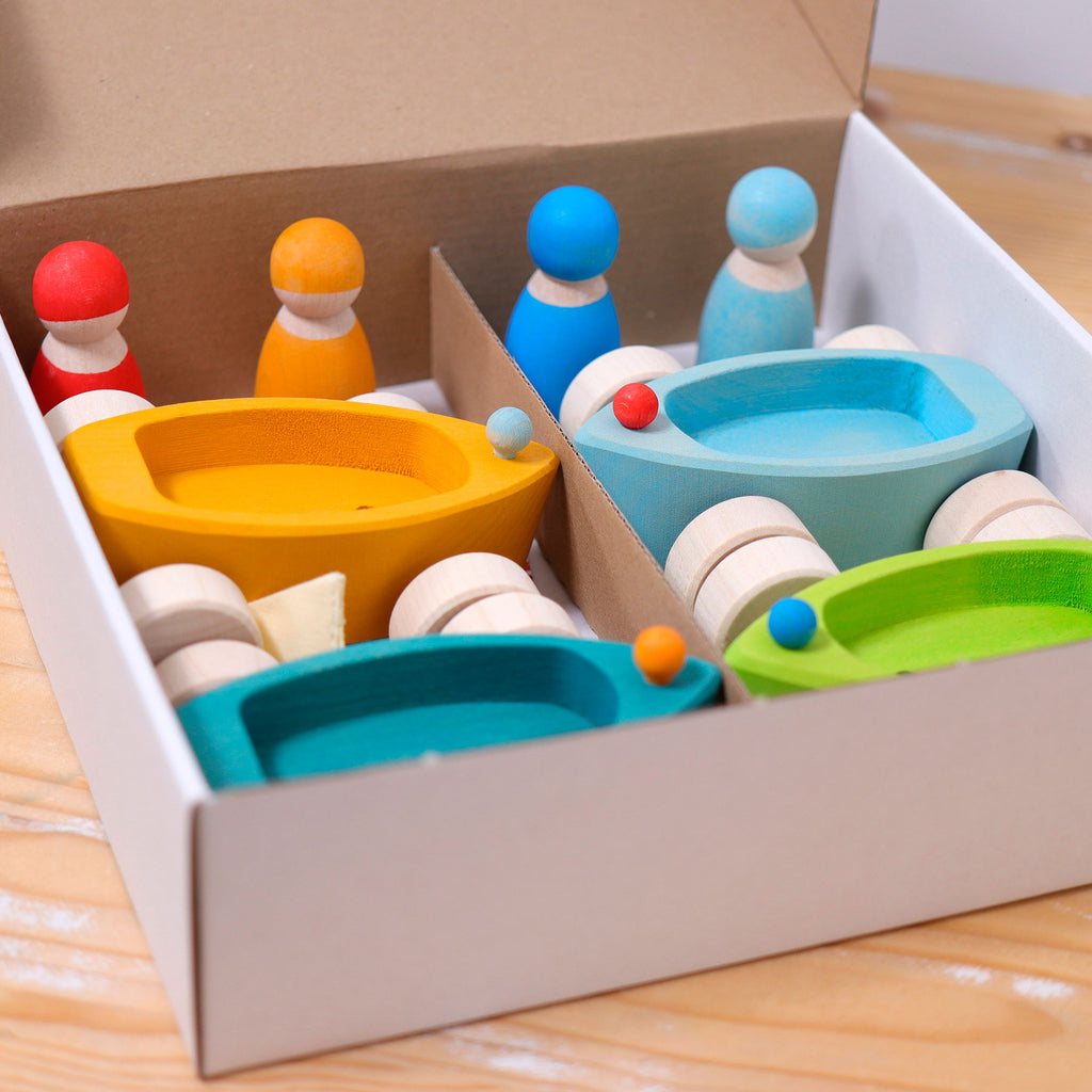 Colorful wooden toy set with boats and figures in a box on a wooden surface