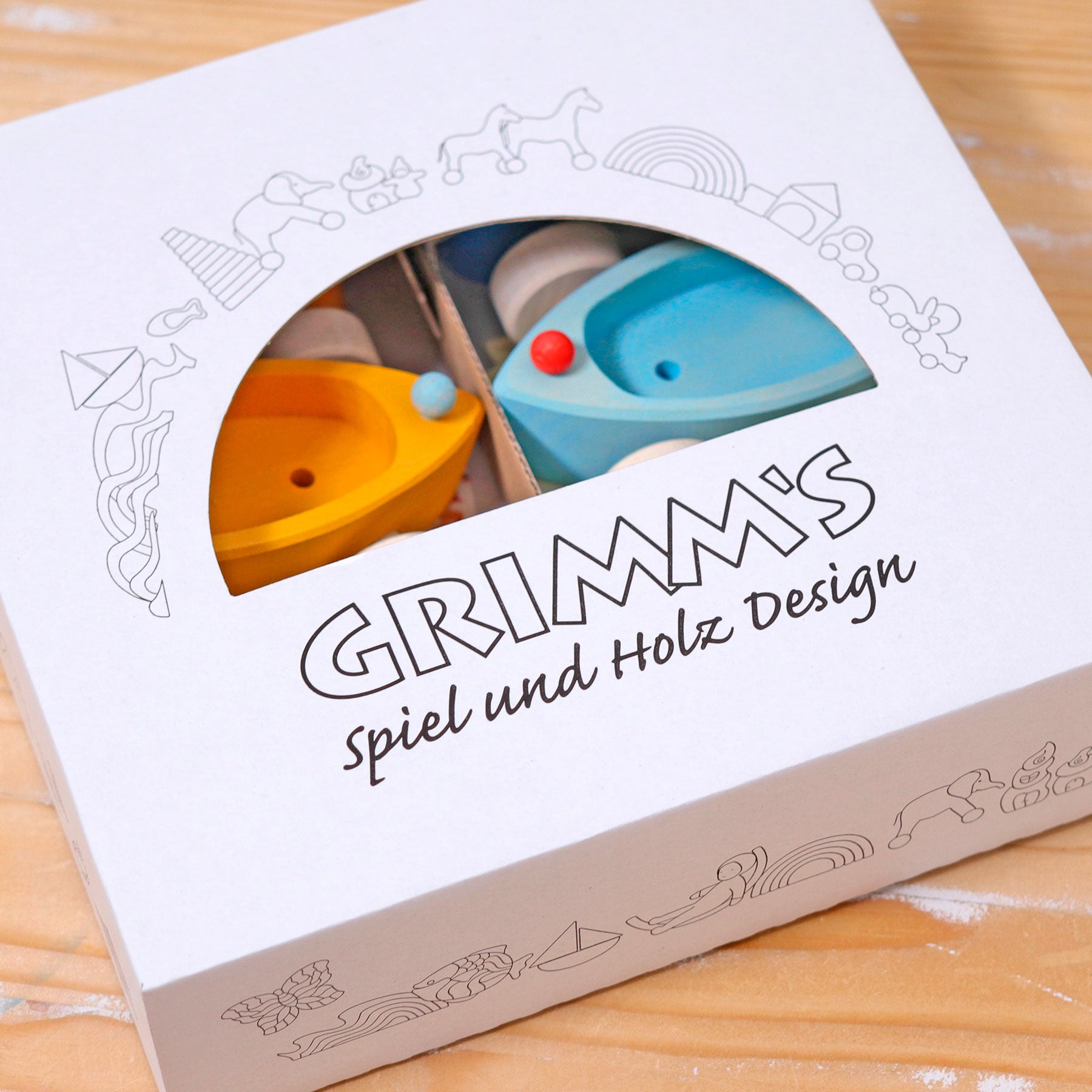 Wooden toy packaging with 'Grimm's Spiel und Holz Design' branding on a wooden surface.