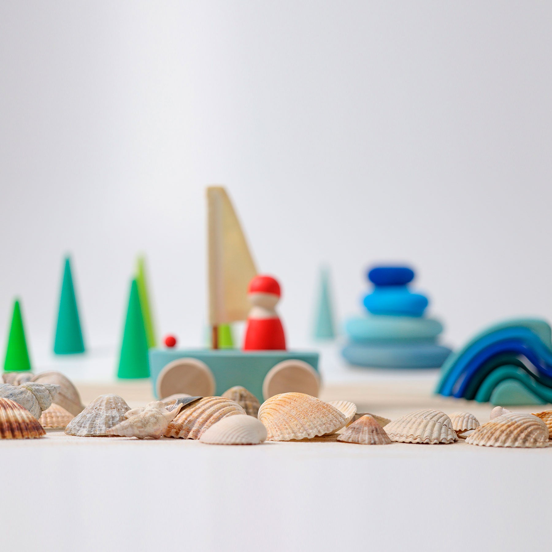 Toy sailboat and colorful trees with seashells on a white surface