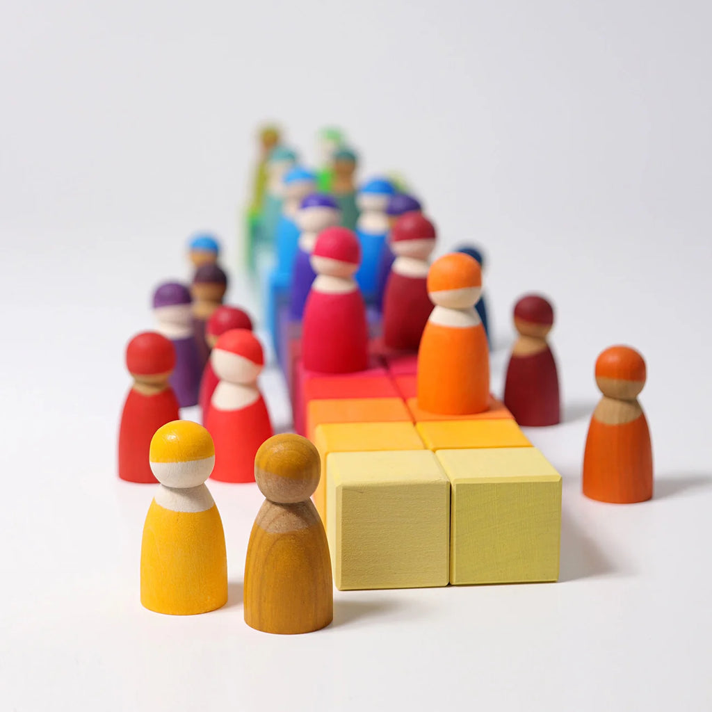 A set of colorful wooden toy figures and blocks arranged on a clean white background. The figures are painted in various colors including yellow, orange, red, blue, and purple, while the blocks are in shades of yellow, orange, and red.