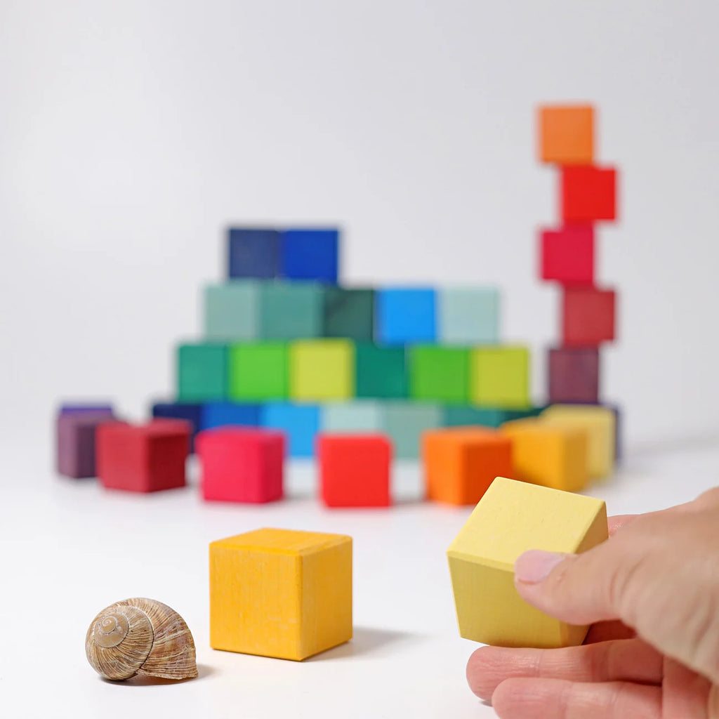 Colorful building blocks with a hand holding a yellow block against a white background