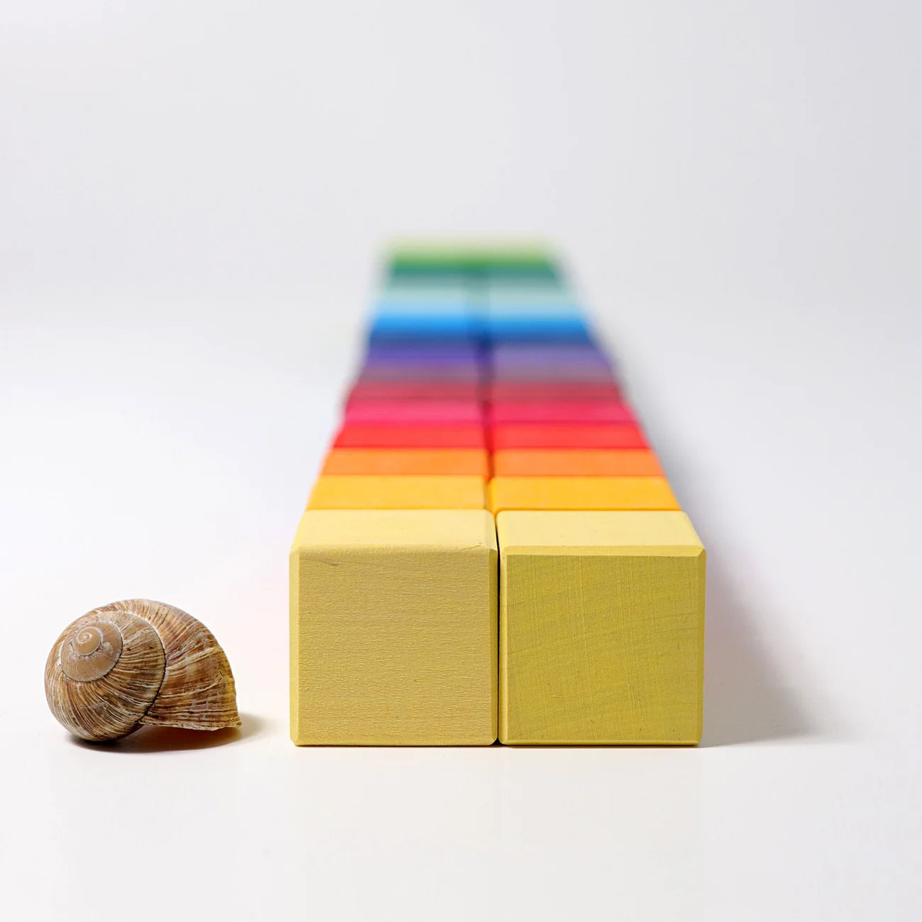 Colorful wooden blocks arranged in a pyramid shape with a small shell on a white background