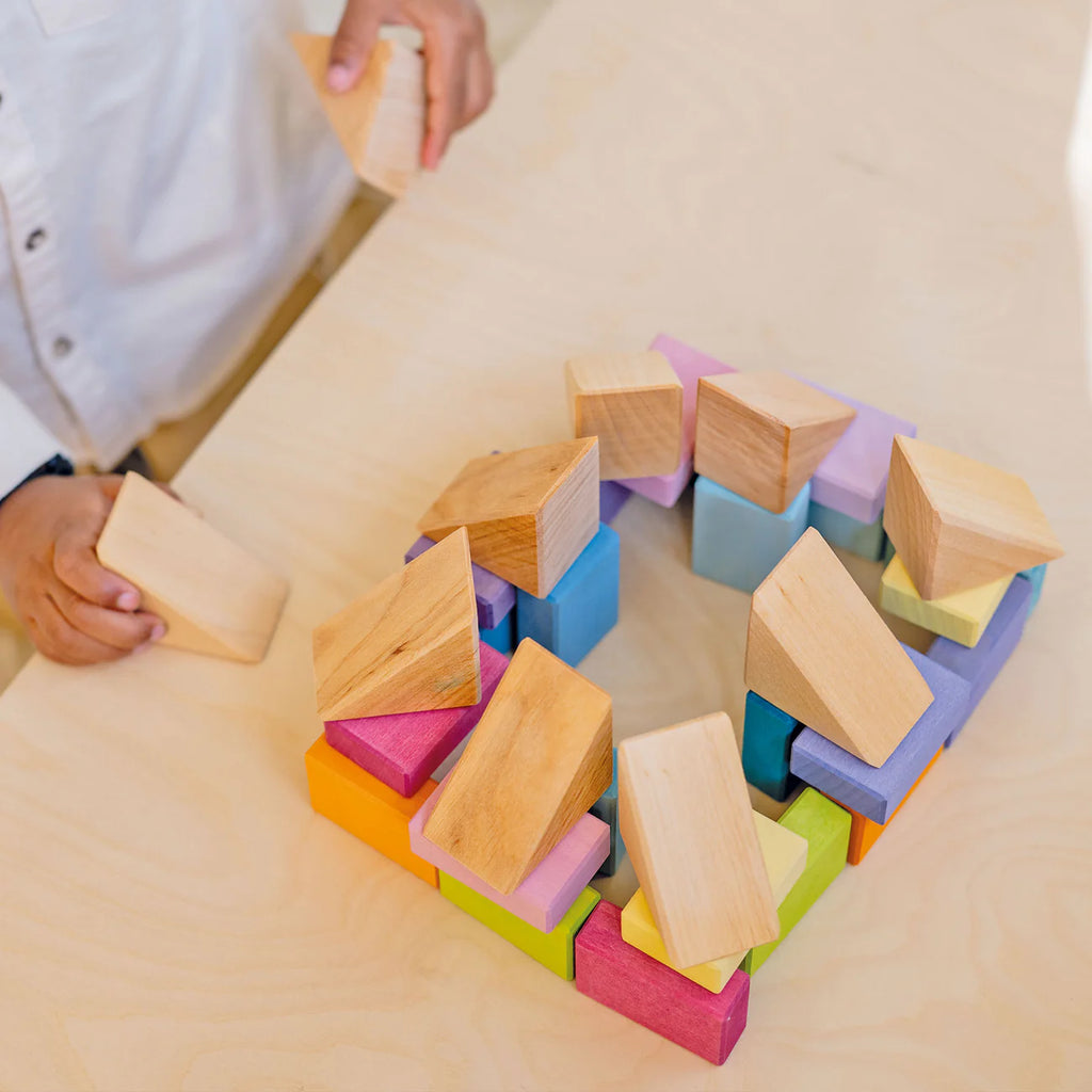 Colorful wooden building blocks being assembled on a light surface.