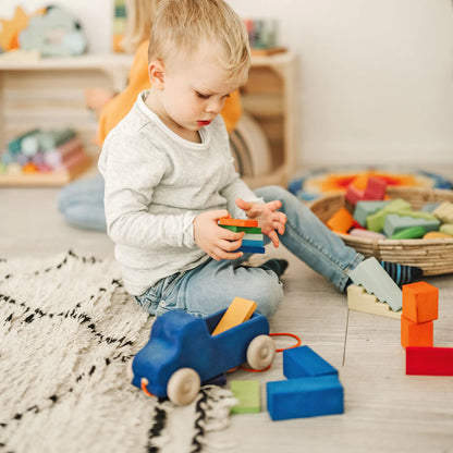 Child playing with colorful blocks on a wooden floor in a room filled with toys.
