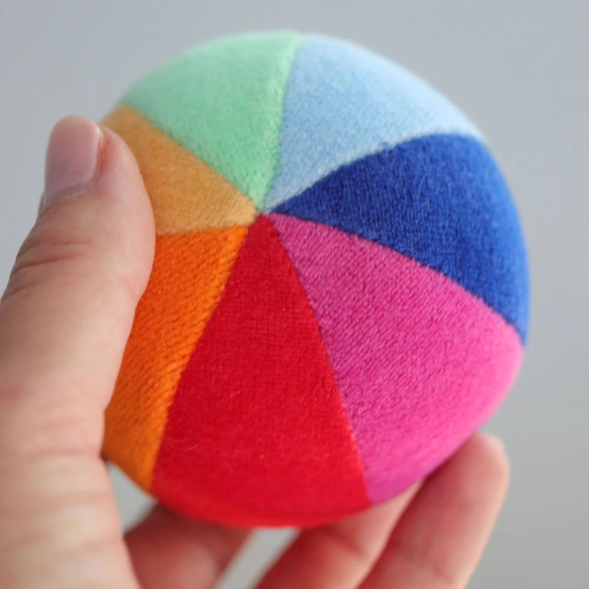 Colorful ball with rainbow pattern held by a hand against a neutral background
