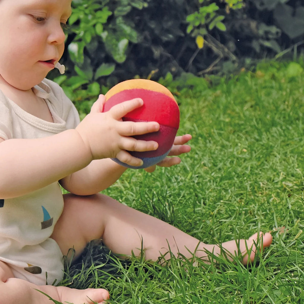 Child holding a colorful ball in a grassy outdoor setting