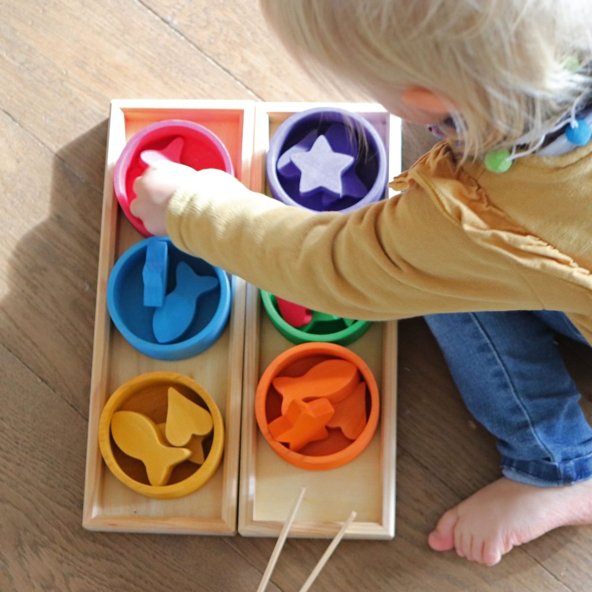 Child playing with a colorful sorting toy on a wooden floor