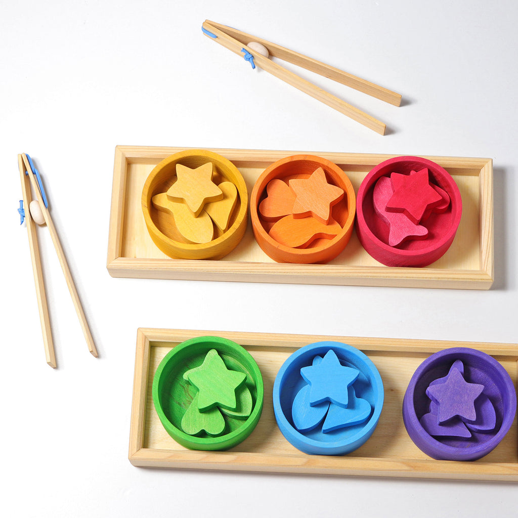 Colorful star-shaped wooden toys with wooden trays and tongs on a white background