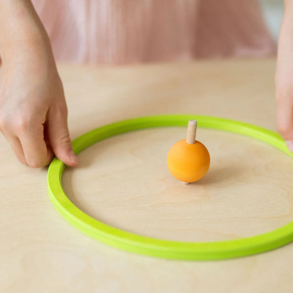 Person attempting to place a green ring around an orange ball on a wooden surface