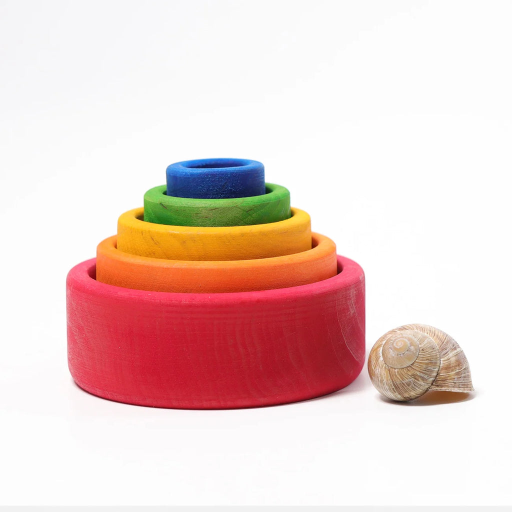 Set of colorful wooden rings stacked on a white background with a shell beside them.