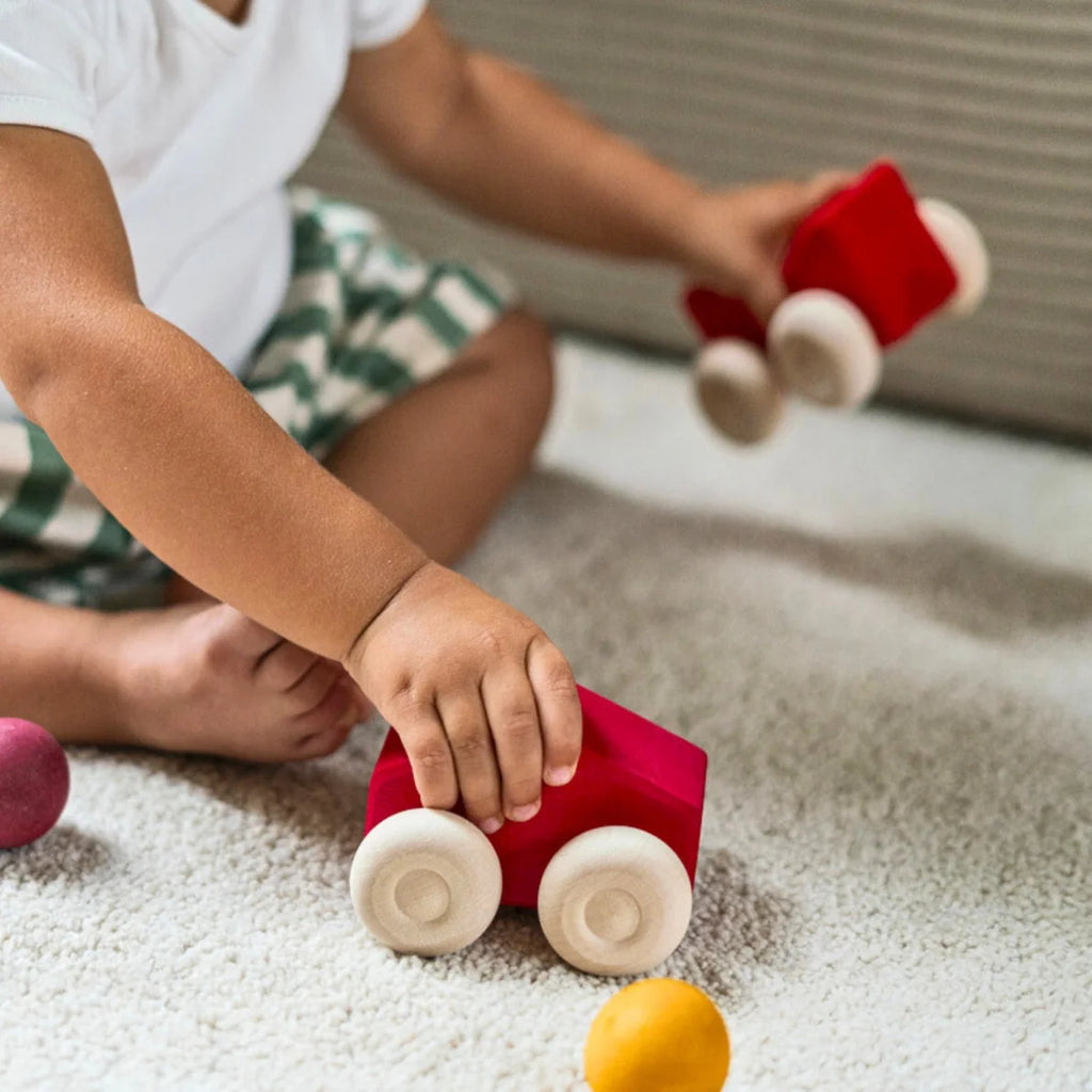 Child playing with red toy car on a carpeted floor