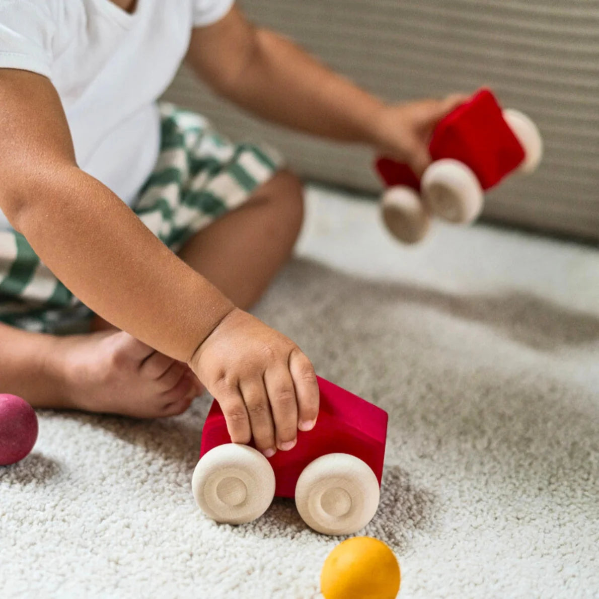 Child playing with red toy car on a carpeted floor